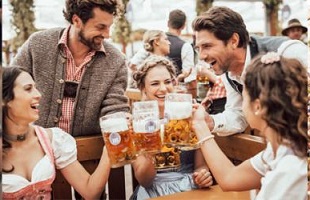 Gruppe junger Menschen in Tracht stößt mit Maßkrügen im Biergarten an, fröhliche Stimmung beim Feiern im Hofbräuhaus-Ambiente.