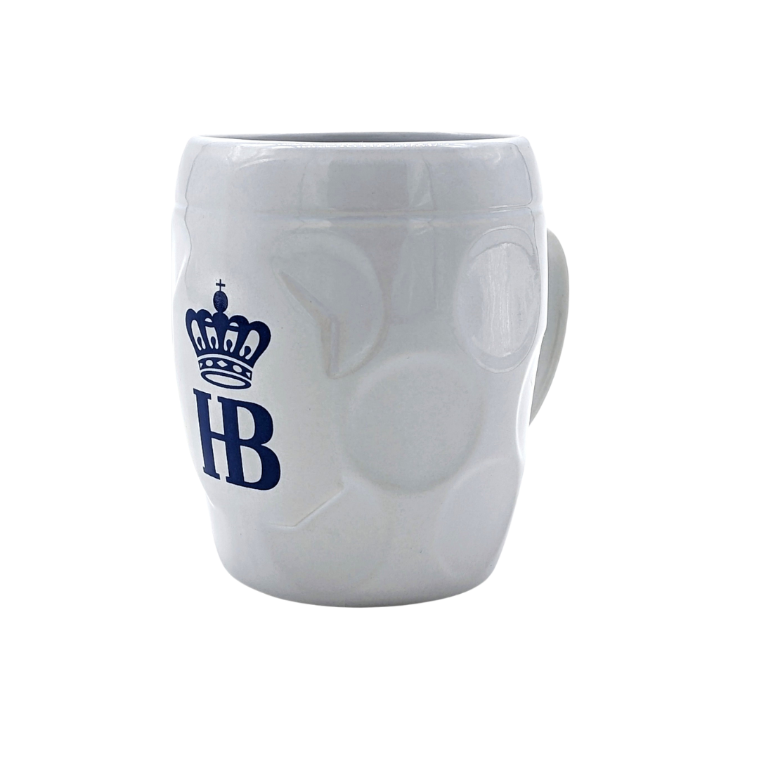 „Weiße Keramiktasse mit strukturierter Oberfläche und kreisförmigen Vertiefungen, blaue ‚HB‘-Krone-Logo auf der Vorderseite, Henkel rechts sichtbar.“