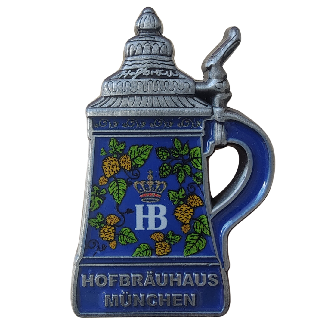Metallischer Pin in Form eines Reliefkrug mit Zinnspitzdeckel, mit emaillierter Oberfläche, verziert mit gelben Hopfen, grünen Blättern und blauem Hintergrund. Mittig das „HB“-Logo mit Krone und der Schriftzug „Hofbräuhaus München“ am Krugboden.