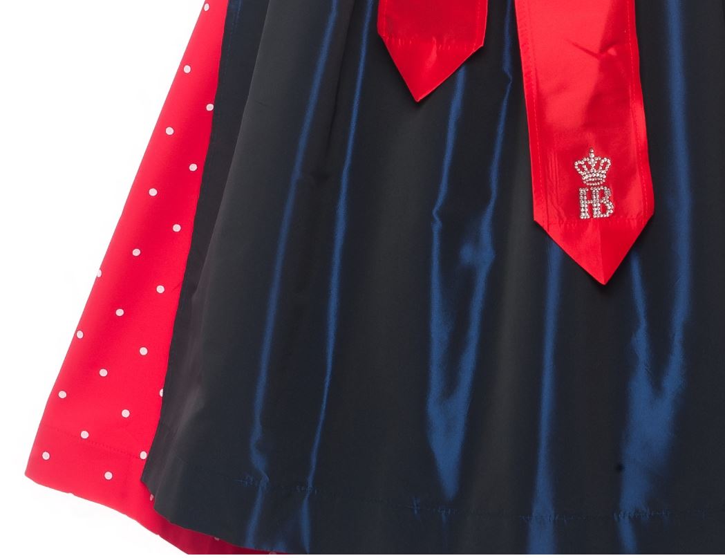 Detailansicht Dirndl Maibock: Rote Schleife mit Strassverzierung des Hofbräuhaus-Logos über dunkelblauer Schürze, daneben roter Rock mit weißen Punkten.